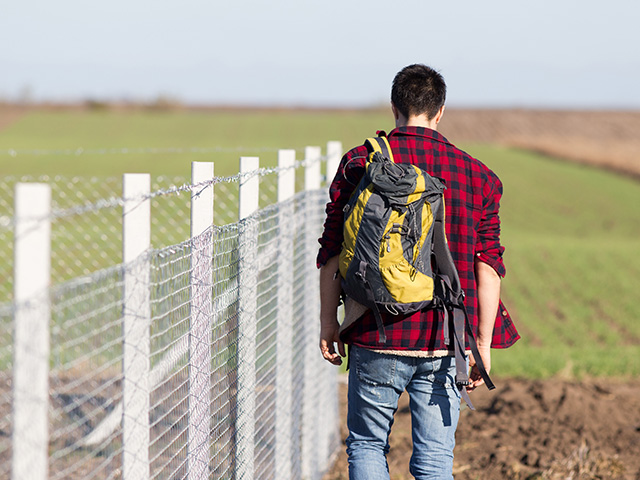 Young man with backpack walking beside fence 640 480px