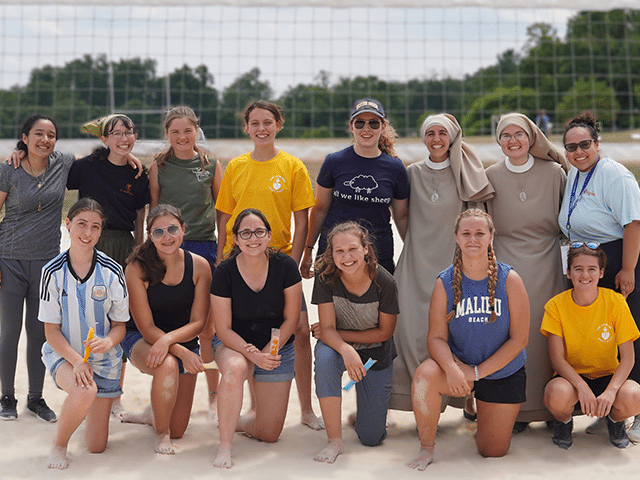Young women with sisters on beach volleyball court